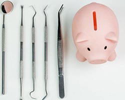 A pink piggy bank and dental tools set against a white background