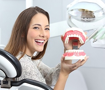 a person smiling and holding a full denture model
