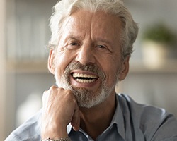 An older man wearing a button-down shirt and smiling after receiving his dental implants