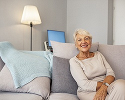 An older woman seated on a couch and showing off her new and improved smile