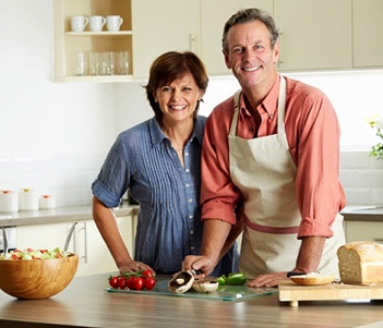 An older couple smiling and preparing a meal