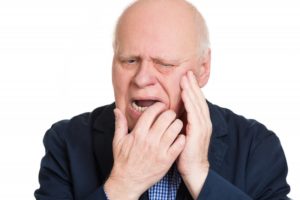 Pained man with hand on cheek has damaged dentures