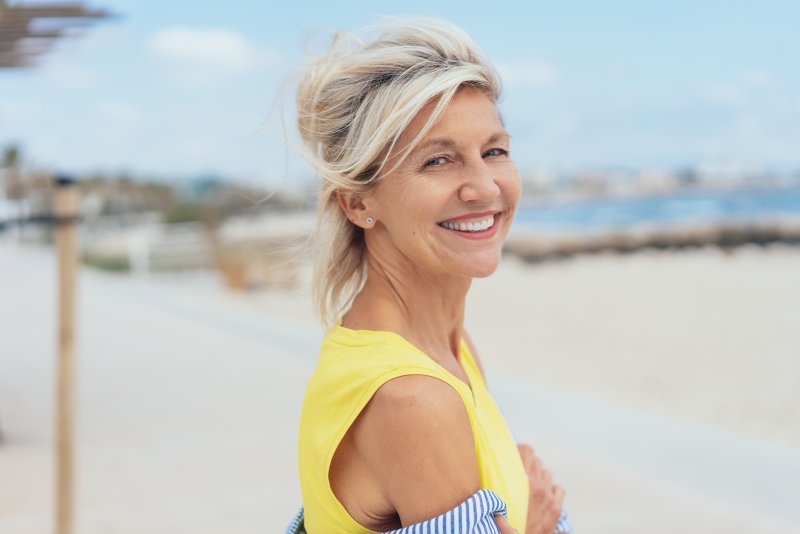 an older woman wearing a yellow blouse overlooks the beach while showing off her dental implants in Vero Beach