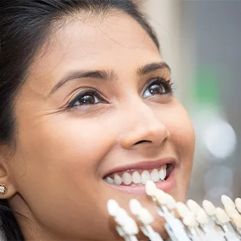 Dentist holding a veneer in front of a patient's smile