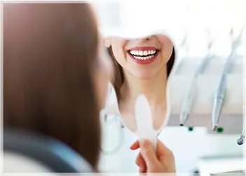 Smiling woman's enhanced smile and teeth reflecting in dental mirror.